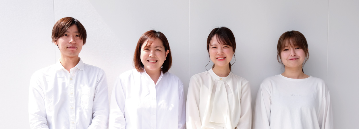 伊勢屋コンサルタントで実際に働いているメンバーの一員である男女4人が白い壁をバックに笑顔で並んでいる写真